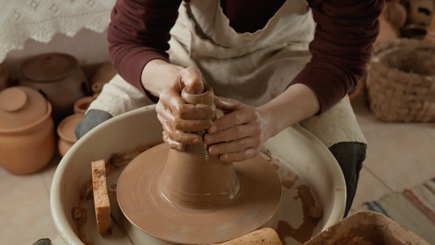 Potter's hands covered with clay making beautiful vase. Man potter working on potters wheel making ceramic vase from clay. Potter at work. Close-up in 4K, UHD Royalty-Free Stock Footage #1104362381