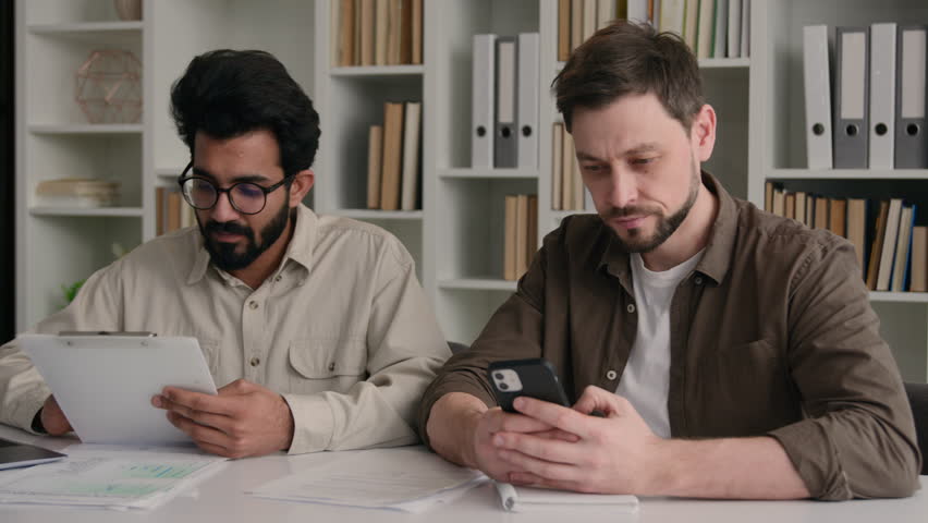 Multiracial men businessmen in office Indian Arabian leader mentor showing business project on laptop talk with Caucasian man indifferent ignoring use mobile phone addiction misunderstanding problem Royalty-Free Stock Footage #1104363997