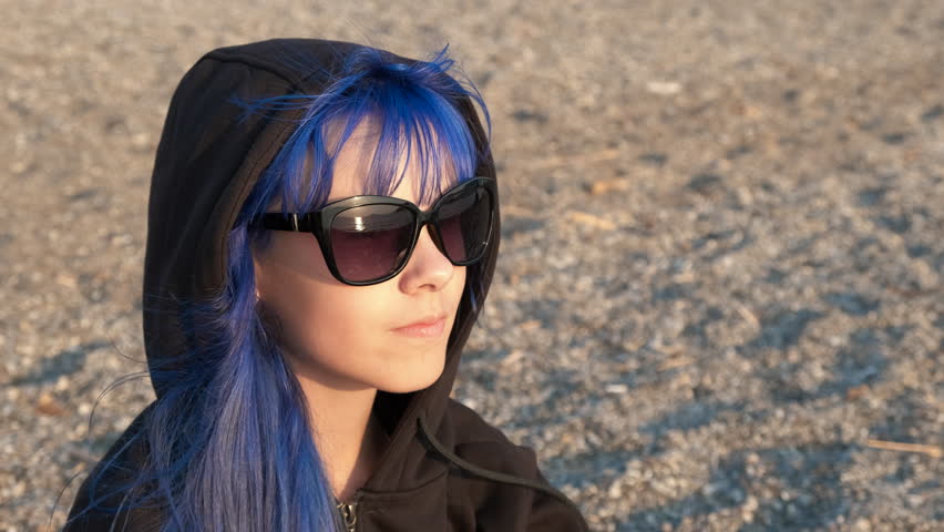 Blue teen in sunglasses on shore. A stressed young girl with blue hair in sunglasses wait for somebody on sunny beach in summer.