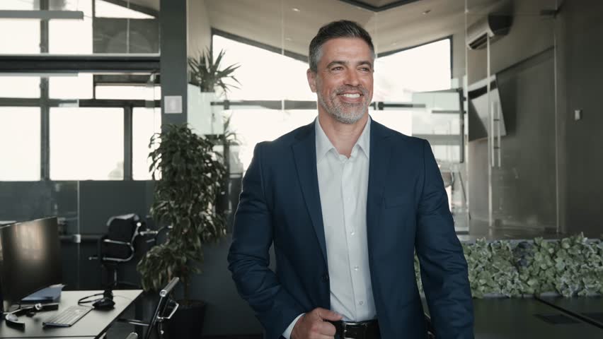 Happy middle aged business man ceo walking in office. Smiling mature confident professional executive manager, businessman owner leader wearing blue suit going along corporate space.