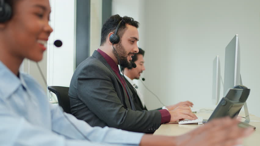 Customer service executive working at call center office. Call center people sitting in front of computer with headphone and talk to customer. Looking on computer screen and happy answer.
