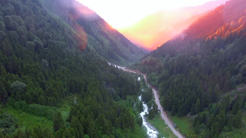 Aerial view of long deep valley with dark forest in mountains illuminated by red sun lights.
