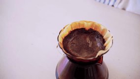 Crop video of professional woman barista, hand pouring hot water on ground coffee over the paper filter on a glass dripper. An alternative method is called Dripping.