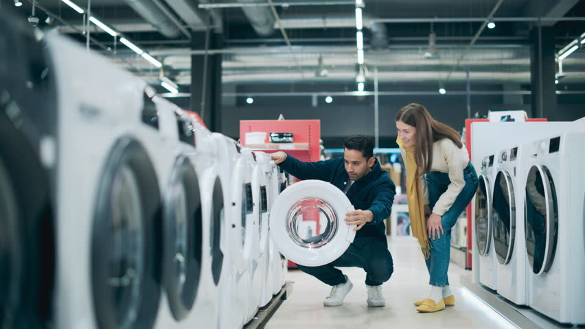 Multicultural Couple Evaluates Washing Machine Choices at Home Electronics Store. Man and Woman in Search of a Reliable Laundry Appliance. Customers Explore Modern Laundry Solutions in a Retail Shop