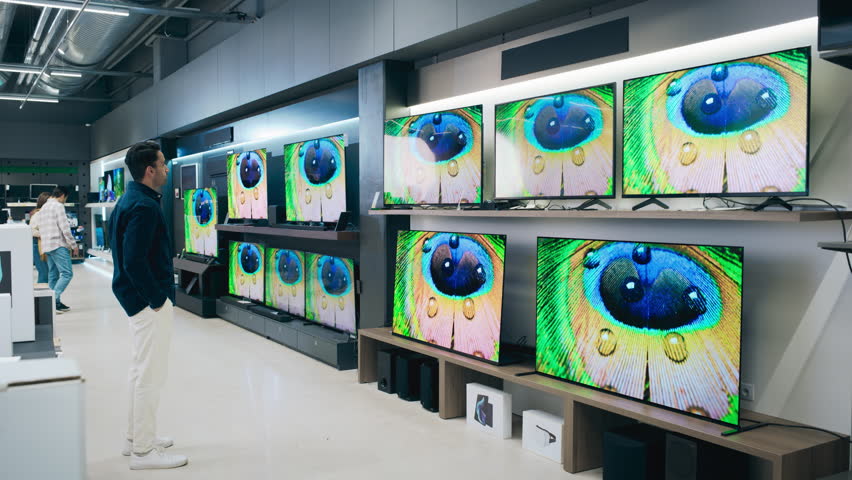 Portrait of a Stylish Man Looking at a Variety of Modern Smart TV Sets with High Quality Resolution Displays and Vivid Color Transmission. Client Shopping for a Television in a Home Electronics Store
