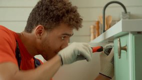 Portrait of concentrated attractive black handyman in protective workwear doing home DIY, repairing broken kitchen cabinet, and fixing tapping screws using screwdriver indoors. - Powered by Shutterstock - Get 15% off with code: PIKWIZARD15