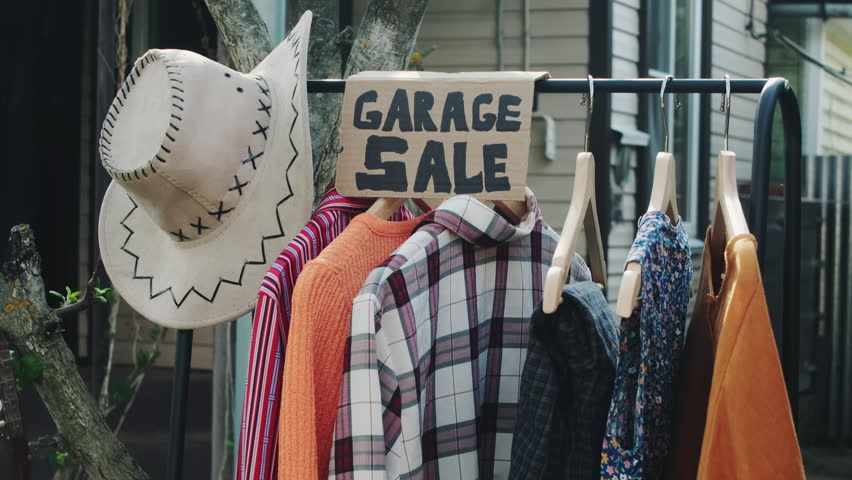 Garage sale concept. Used clothes hang on floor hanger in front yard. Royalty-Free Stock Footage #1104382531