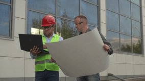 a man in a red helmet looks at the tablet. The worker holds a technical plan in his hands. Slow motion video. High quality Full HD video recordingecording