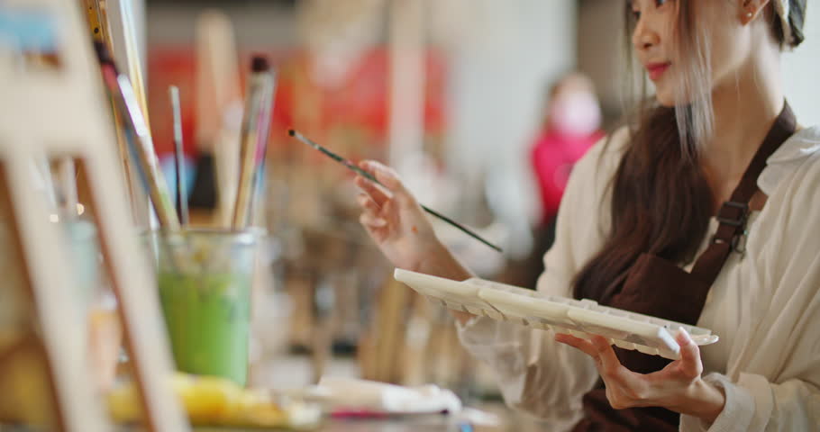 Beautiful asian stylish female artist painting picture in art studio. Young woman painter draws with paint brush and oil colors creating artwork sunset landscape on canvas. imagination and creativity. Royalty-Free Stock Footage #1104387241