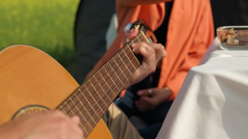 Close view man's hands playing acoustic guitar while girlfried eating chocolate on picnic in rural country field in slow motion Royalty-Free Stock Footage #1104389205