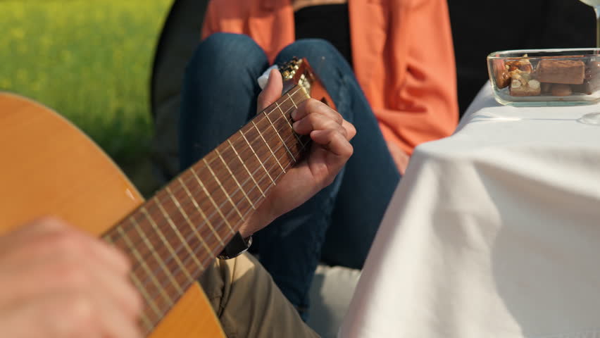 Close-up of man's hands playing chords song on acoustic guitar outdoors to girlfriend on picnic Royalty-Free Stock Footage #1104389587