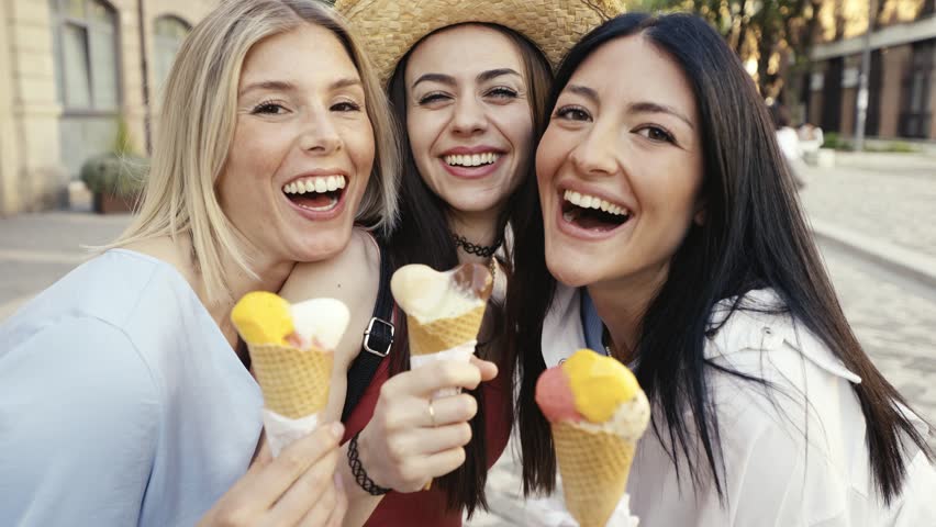 Three cheerful teenage women eating ice cream cones on city street - Happy female tourists enjoying summer vacation in Italy - Summertime holidays