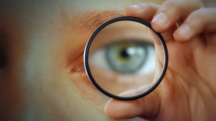 Magnified Eye Hand Holding Glass Front Face. Hand holding a magnifying glass showing eye in front of face, strange scene. Royalty-Free Stock Footage #1104392007
