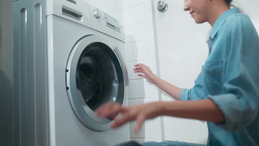 Beautiful Young Asian Woman Put Dirty Clothes into Washing Machine. Happy Asian Girl do housework sits in front washing machine, loads of clothes dirty Laundry at home. Household chore Concept. Royalty-Free Stock Footage #1104400323