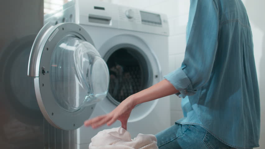 Beautiful Young Asian Woman Put Dirty Clothes into Washing Machine. Happy Asian Girl do housework sits in front washing machine, loads of clothes dirty Laundry at home. Household chore Concept. | Shutterstock HD Video #1104400329