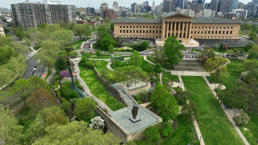 Aerial rotation around Philadelphia Museum of Art and Fairmount Park. City skyline and blue sky behind lush urban green spaces and public musuem in historic city of brotherly love.