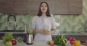 Young beautiful girl tells in kitchen how to make healthy smoothie from fruits and vegetables. Healthy eating ideas. 