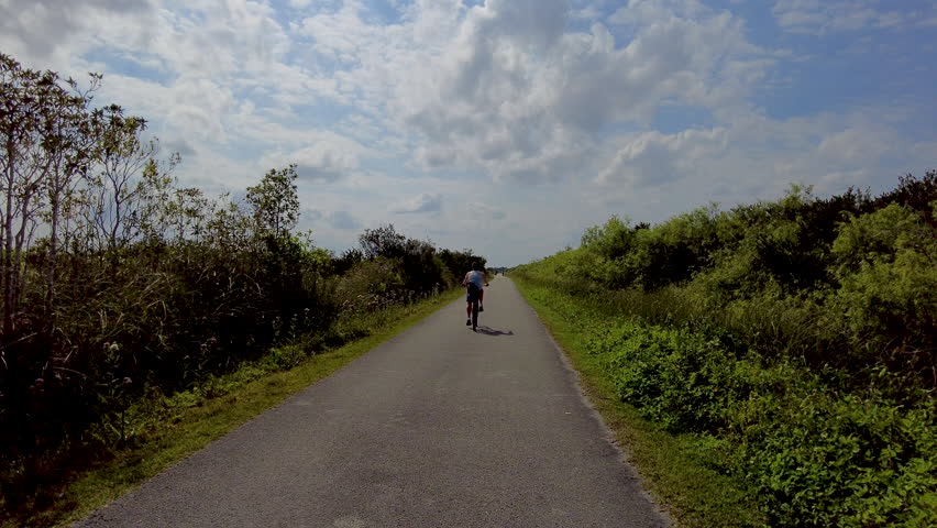 Following Woman Riding Bicycle On Narrow Path in the Everglades
