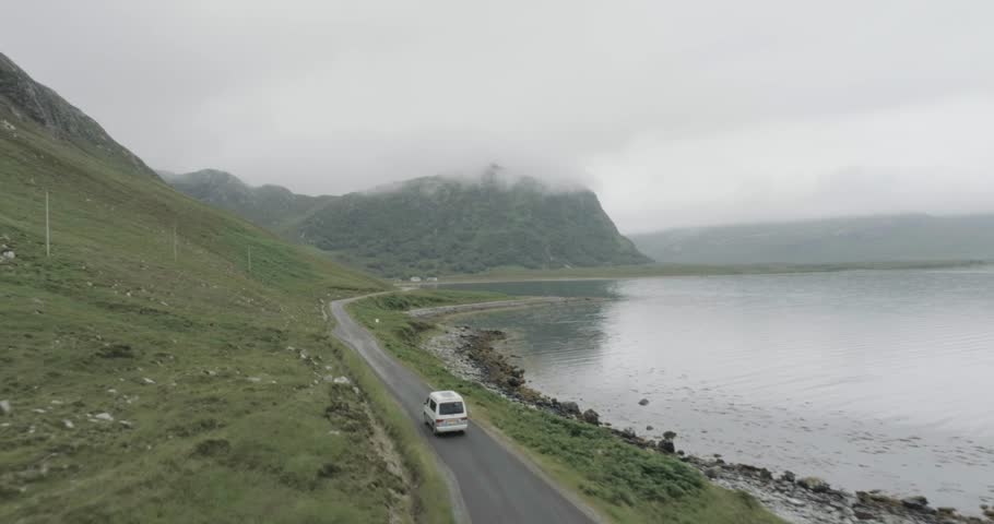 Close up drone tracking shot of a campervan on a single track road during a trip of the Scotland North Coast 500 with a Loch and cloudy topped mountains in view to passing the camper van Royalty-Free Stock Footage #1104410751