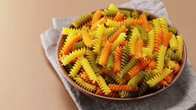 Colorful italian raw pasta on a linen napkin. Tricolor fusilli pasta on a clay plate. Panning camera shot