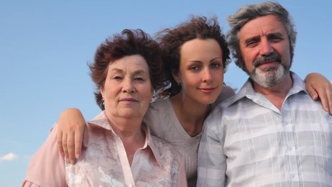mature couple stands embracing with their adult daughter against sky in summer