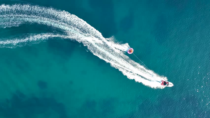 Tubing boat with people moving behind the boat on the water. Aerial view of motor speed boat pulls inflatable rubber raft with people. Summer vacation shot