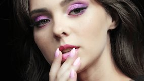 Closeup slow motion video of human female face. Footage of woman with hand near face and nails with pink manicure. Eyes are with pink shaudows beauty makeup.
