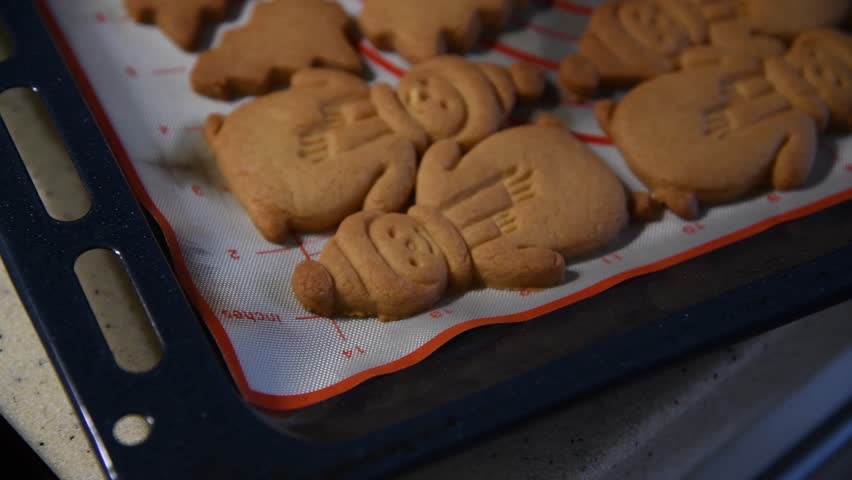 Close-up view of brown baked Snowman and Christmas tree shaped shortbread (or shortie) holidays cookies lying on baking sheet. Soft focus. Christmas food preparation theme. | Shutterstock HD Video #1104415267