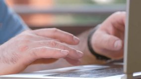 Close-up of hands of unrecognizable businessman typing on laptop keyboard while working at office desk on background of large panoramic window. Concept of office working. Tracking shot in slow motion.