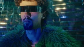 Glamorous man wearing feather jacket and futuristic cyclops sunglasses posing under multicolored neon light on silver foil background. Creative portrait, fashion photoshoot - Powered by Shutterstock - Get 15% off with code: PIKWIZARD15
