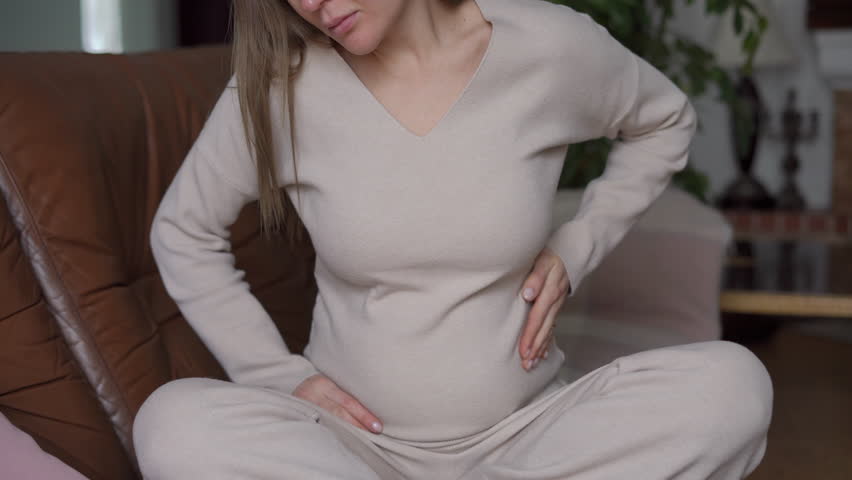 Front view unrecognizable Caucasian pregnant woman stroking belly sitting on couch in living room. Happy relaxed confident future mother caressing unborn fetus at home indoors | Shutterstock HD Video #1104423245