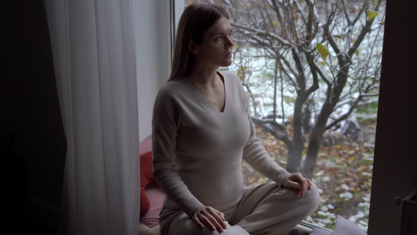 Confident happy pregnant woman closing eyes meditating in lotus pose sitting on windowsill. High angle view portrait of satisfied Caucasian expectant doing breathing exercise at home indoors | Shutterstock HD Video #1104423263