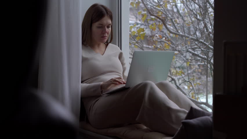 Live camera zoom in to confident happy pregnant woman messaging online closing laptop looking out window. Satisfied Caucasian lady sending email enjoying leisure sitting on windowsill | Shutterstock HD Video #1104423269