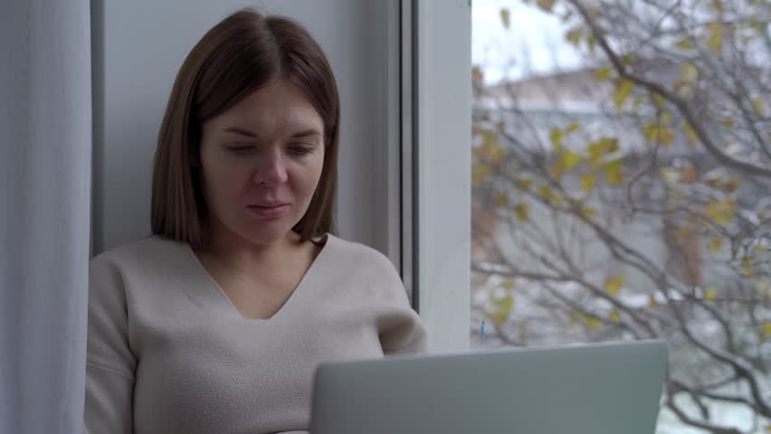 Portrait of positive pregnant woman sending email closing laptop looking out window. Happy confident satisfied Caucasian expectant sitting on windowsill at home indoors | Shutterstock HD Video #1104423275