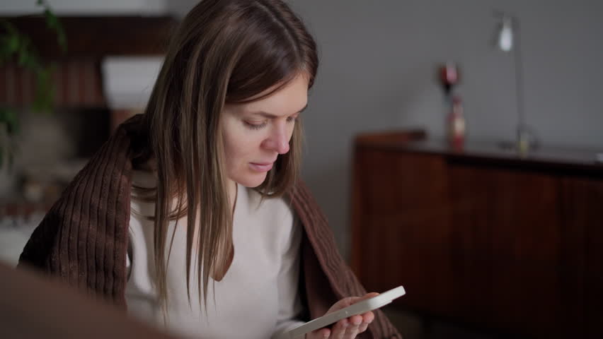 Joyful charming young woman laughing watching online video in smartphone app. Portrait of happy carefree Caucasian millennial lady enjoying leisure at home indoors | Shutterstock HD Video #1104423295