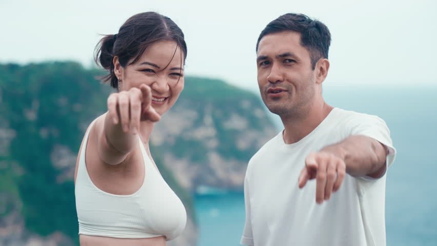 Asian people finger point at camera and laughing. Happy Korean couple. Travel moments for happy family on a rock seaside on summer holiday. Vacation on ocean shore. Man and woman positive emotion. | Shutterstock HD Video #1104424567