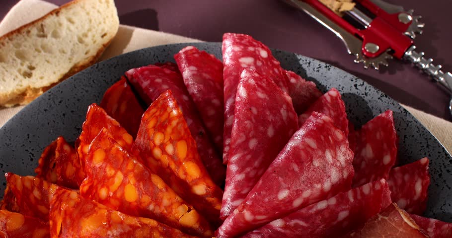 Meat slices on a plate. traditional spanish sausage with beef jerky. salchichon, chorizo and prosciutto with glass of wine. serving cold cuts with dried tomatoes and bread. antipasto in sunlight. | Shutterstock HD Video #1104426929