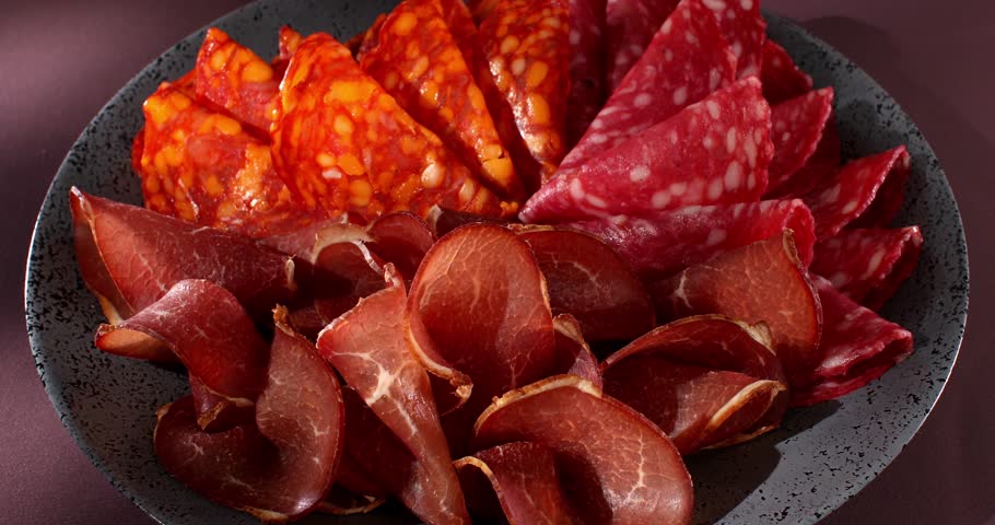 Meat slices on a plate. traditional spanish sausage with beef jerky. salchichon, chorizo and prosciutto with glass of wine. serving cold cuts with dried tomatoes. antipasto in sunlight. | Shutterstock HD Video #1104426933