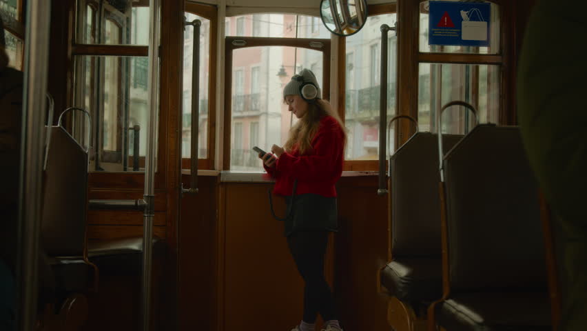 Young beautiful woman in tram or bus look out of rear window. Cinematic authentic shot of millennial youth use public transport, listen to music and scroll through phone. Concept travel solo