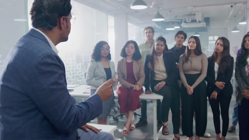 A middle aged Indian Asian confident male entrepreneur or businessman is communicating or discussing with his team members or employees during a group meeting in a modern corporate start up office | Shutterstock HD Video #1104433633