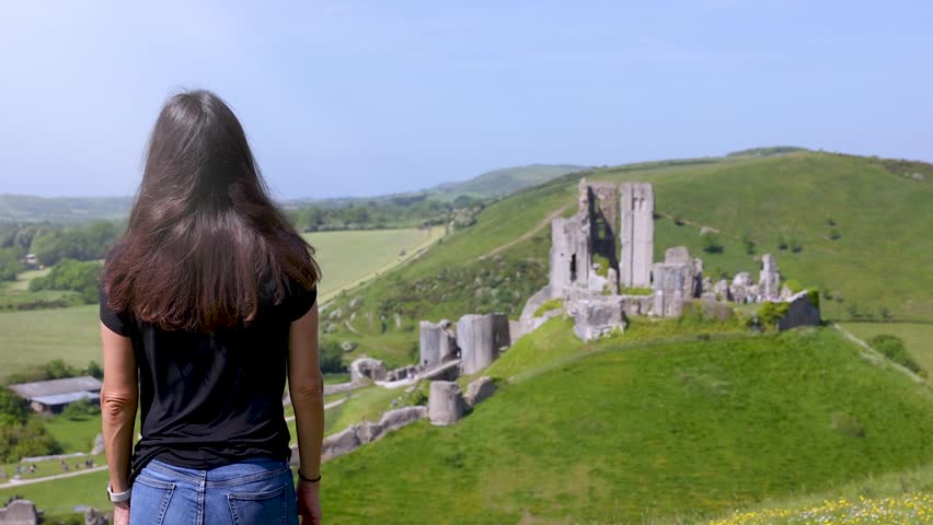 A tourist woman looks at the ruins of Corfe Castle, Dorset, England, during a sunny spring day