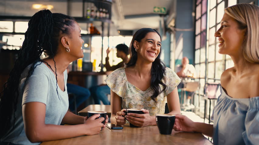 Group of multi-cultural female friends meeting in restaurant or coffee shop looking at social media on mobile phone and laughing together - shot in slow motion Royalty-Free Stock Footage #1104443929
