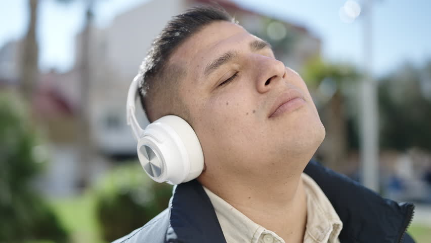 Young hispanic man listening to music at park