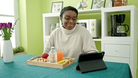 African american woman having breakfast using touchpad at dinning room