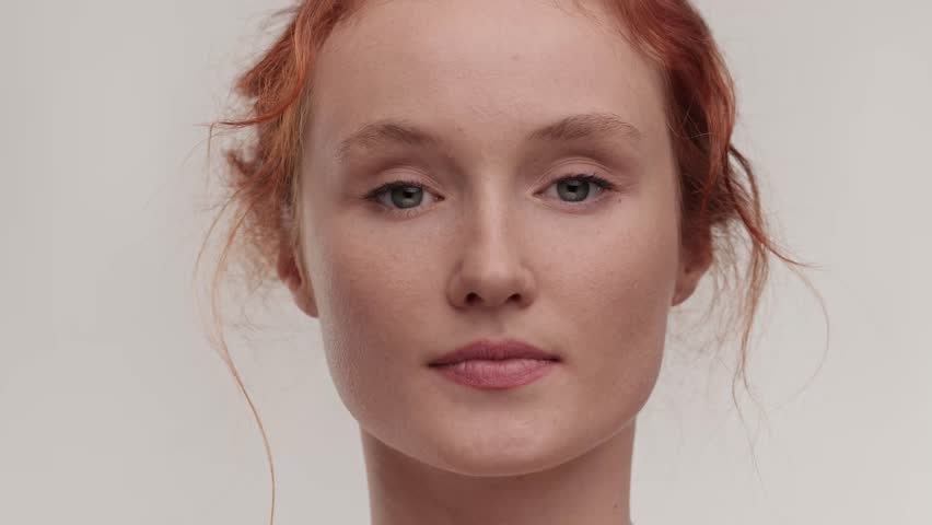 Beautiful caucasian model ginger girl touching her eyes. Natural cosmetics. Portrait of millennial female model with naked shoulders and nude make up posing . Concept of cosmetology, skincare