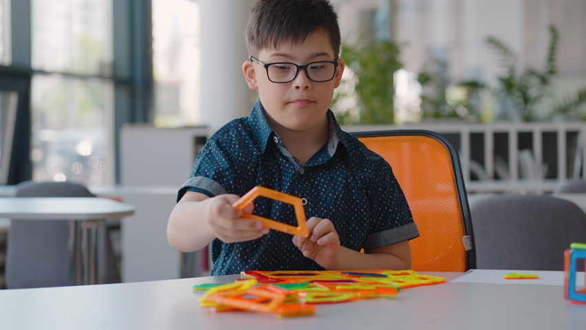 School boy with Down syndrome, plays with lots of colorful plastic blocks constructor, building figure. Fine motor skills development, kids entertainment. Education concept. People. School life | Shutterstock HD Video #1104459323