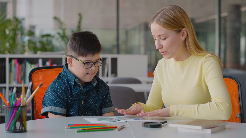 Educational psychologist work with a Down syndrome child boy, shows him educational cards to develop his associative thinking. Special education and psychological test for children with disabilities | Shutterstock HD Video #1104459337