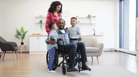 Full length view of african american parents showing their care while embracing smiling kids in studio apartment. Handsome father with disability telling jokes and making little boys laugh at noon. - Powered by Shutterstock - Get 15% off with code: PIKWIZARD15