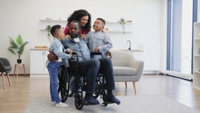 Full length view of african american parents showing their care while embracing smiling kids in studio apartment. Handsome father with disability telling jokes and making little boys laugh at noon. - Powered by Shutterstock - Get 15% off with code: PIKWIZARD15