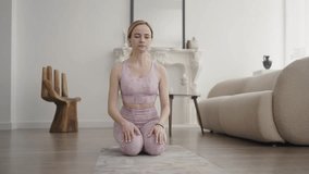 Young girl performs yoga stretching exercise on a rug in a bright room. Girl watches online lesson on laptop. Slow motion